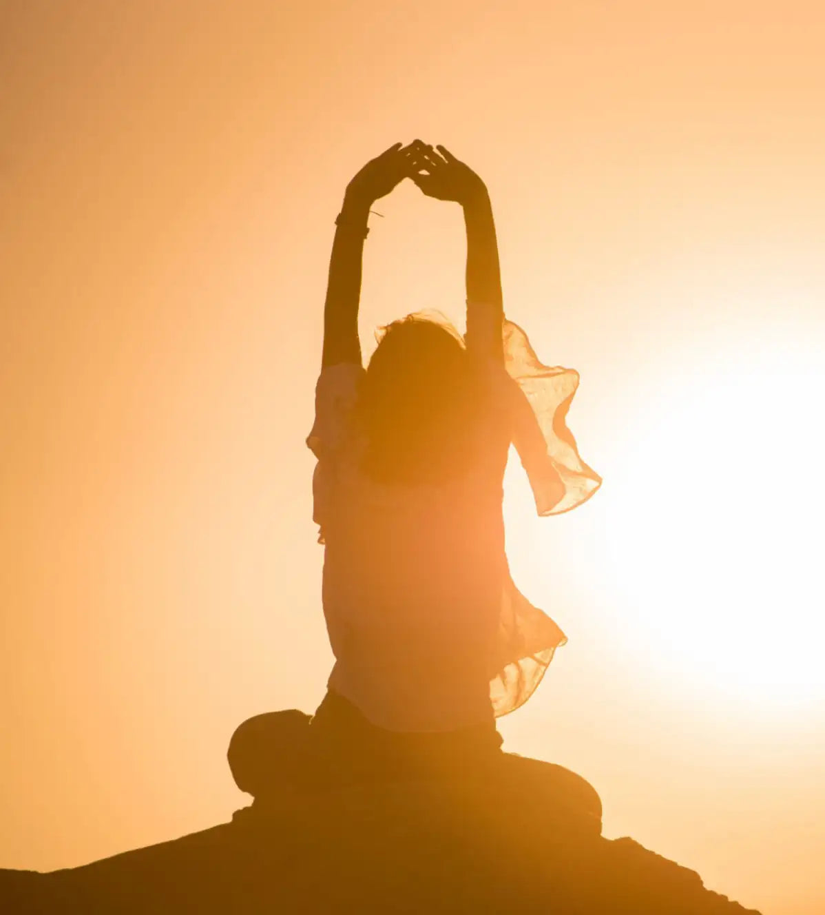 Silhouette of a person in flowing, translucent fabric against a warm orange sunset.